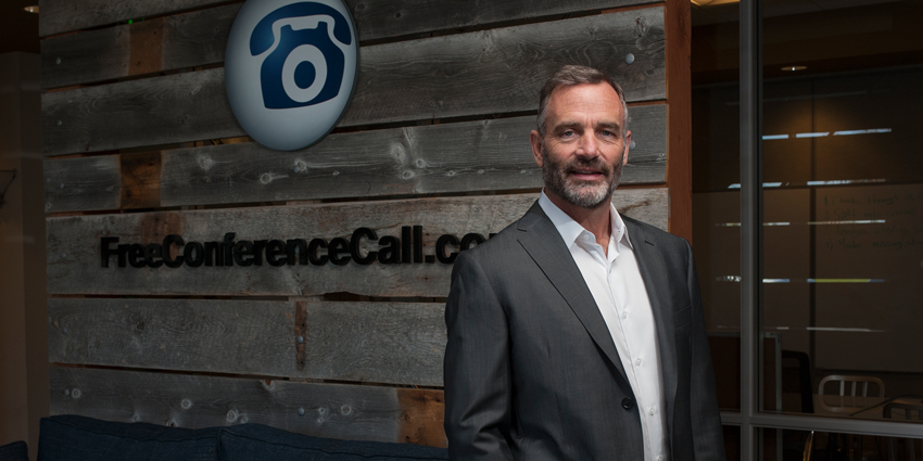 FreeConferenceCall.com CEO Dave Erickson standing in office alongside logo