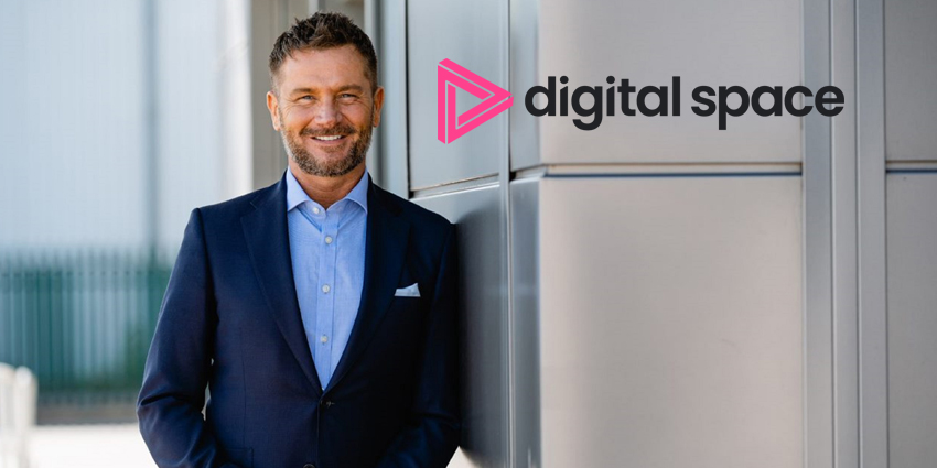 Neil Muller looking at camera, leanging against exterior wall with Digital Space logo beside him