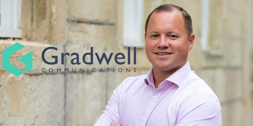 Jamie Ward standing against sandstone wall with arms crossed with Gradwell logo