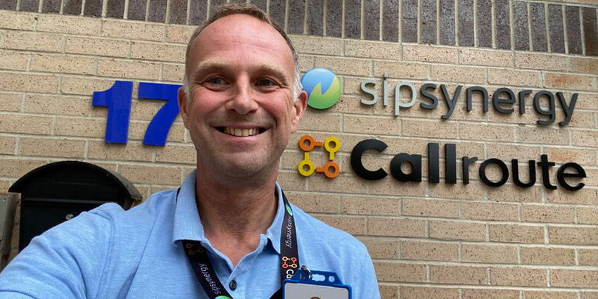 Ewan Haig selfie taken outside Callroute office with latter's logo and Sipsybergy logo on the brown exterior office wall behind him