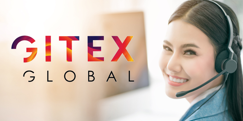 Asian woman with headset and in front of computer smiling over her shoulder at camera with GITEX Global logo beside her