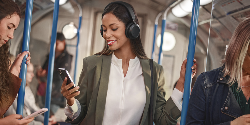 Black woman on tube wearing Jabra Evolve2 75 headset and smiling at her phone