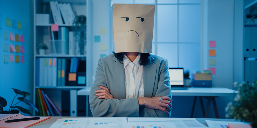 Hybrid worker at his desk with a bag over his head drawn with a sad face